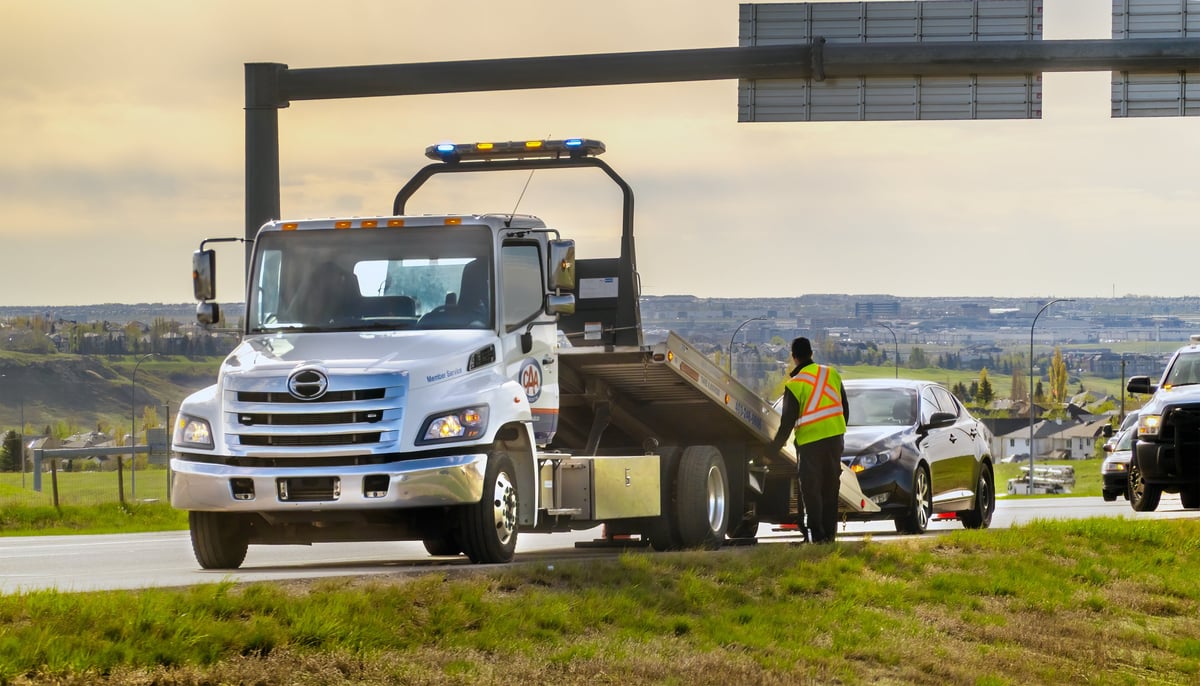 Tow truck assisting a broken-down vehicle on a highway shoulder